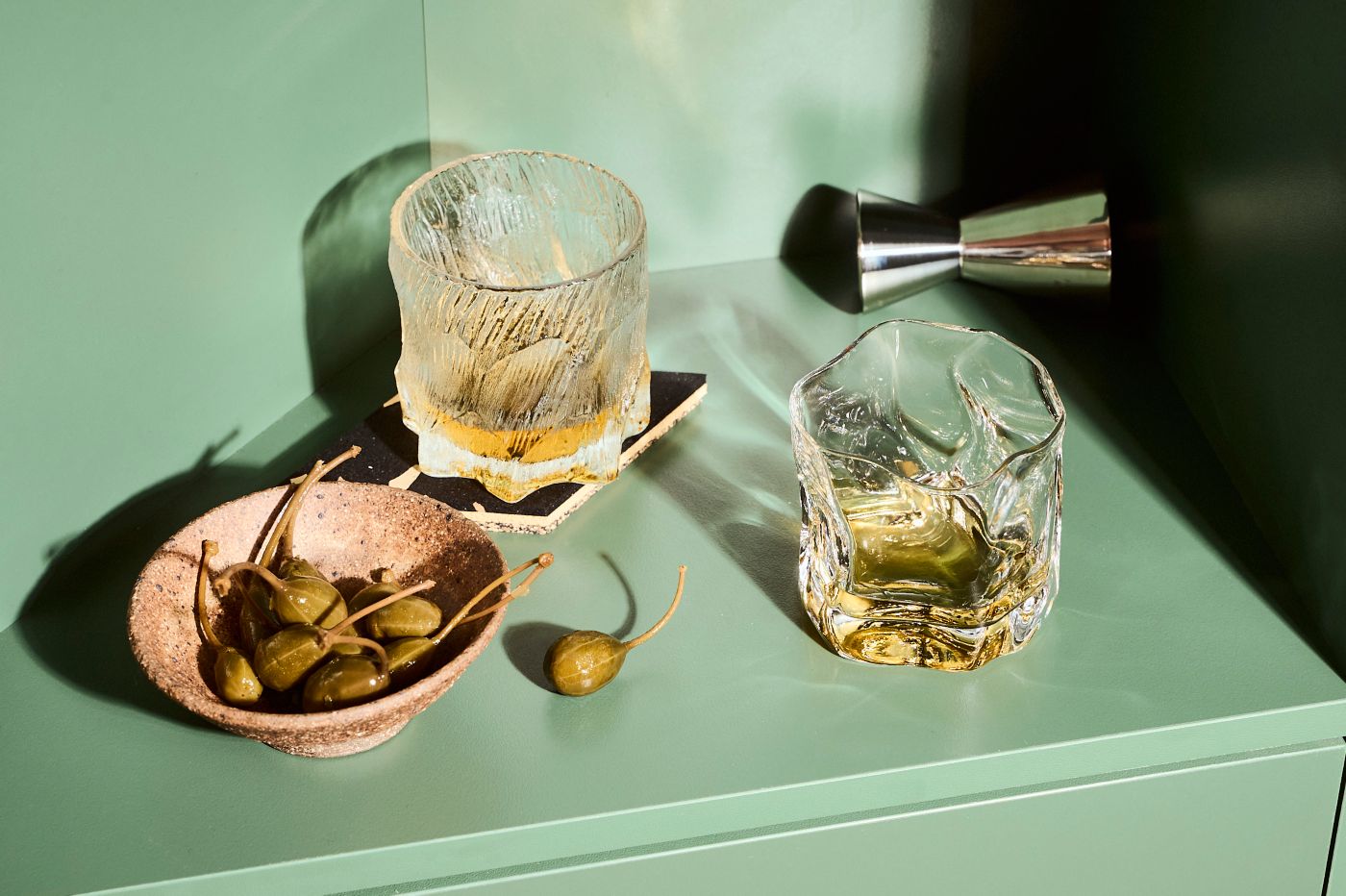 A couple of glasses of Scotch whisky with olives on a green shelf