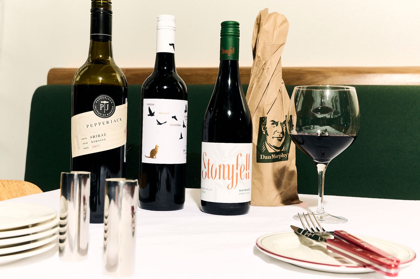 An image of a red wine bottle and a glass along with a set of plate and cutlery on a table