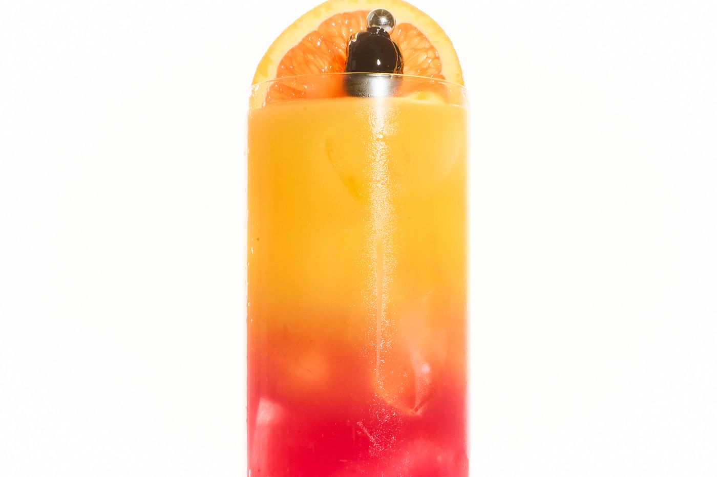 A layered cocktail in a tall glass garnished with an orange slice and cherry