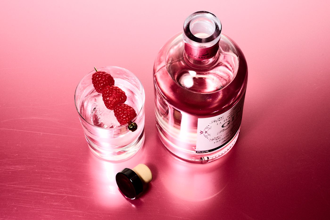 A glass and a bottle of pink gin against a pink background 