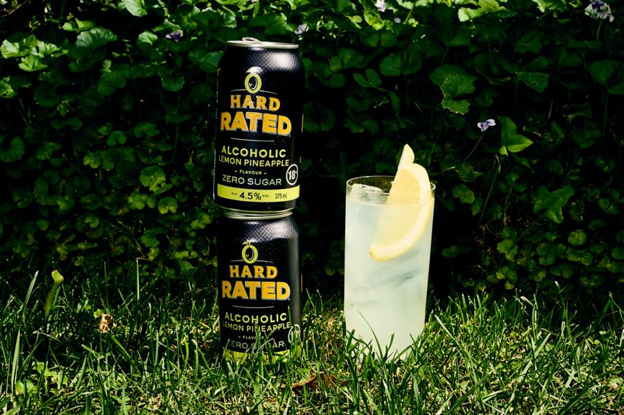 Two cans of Hard Rated Lemon Pineapple on the grass with a glass of the new drink