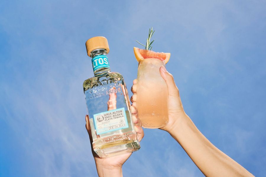 Holding up a bottle of Altos Tequila and a Paloma cocktail