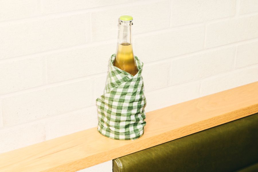 A bottle of wine wrapped in a tea towel sitting on a bench 