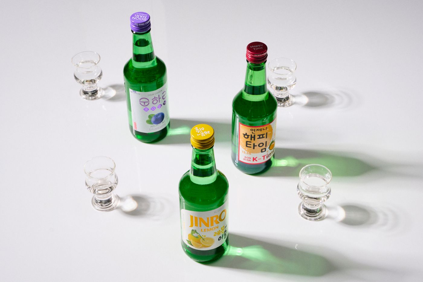 Three bottles of soju with shot glasses next to them