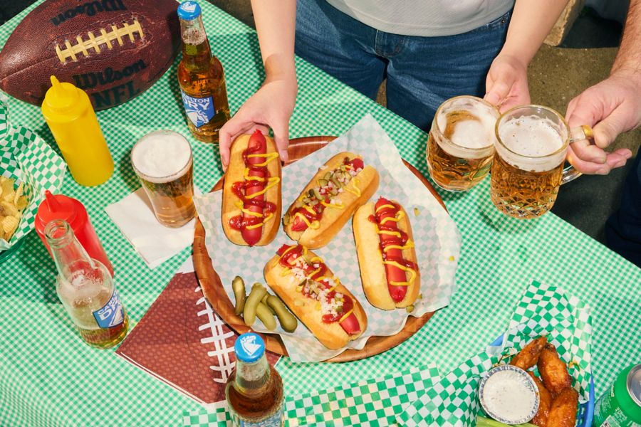 Hot dogs on a table with beers and a football