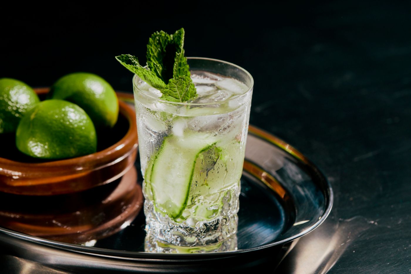 A Gin & Tonic on a tray with a bowl of limes  