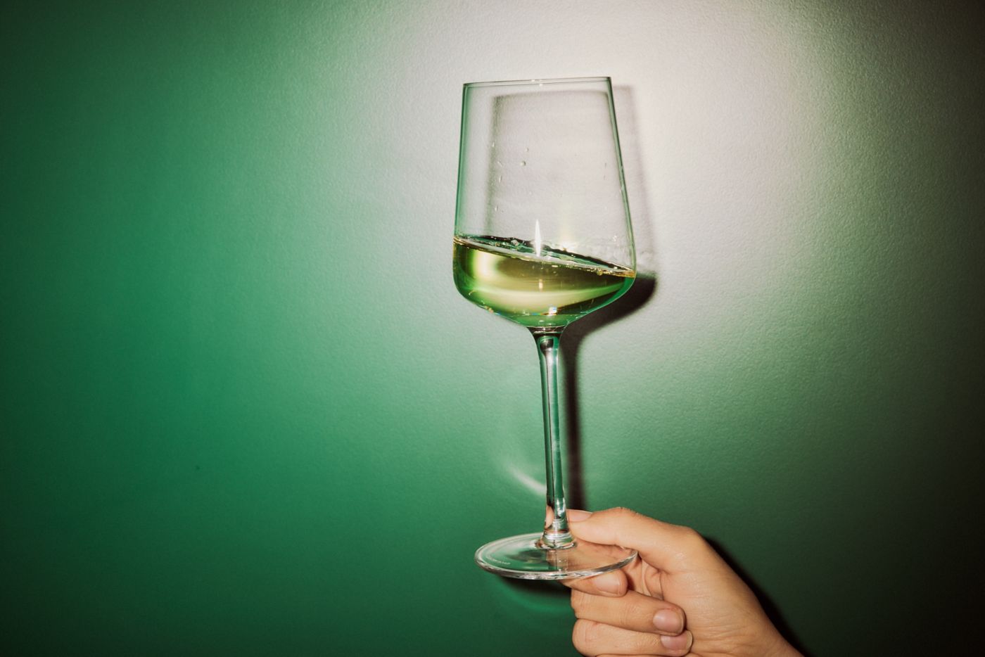 Holding a glass of white wine against a green backdrop